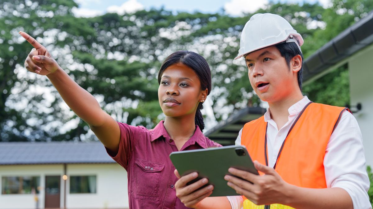 A homeowner points out an area of concern to a roofer holding a tablet outside her home